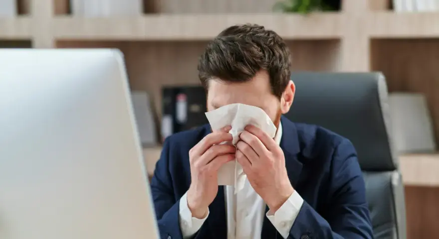 Hombre con traje se suena la nariz con un pañuelo, preocupado por un posible despido por faltar al trabajo.
