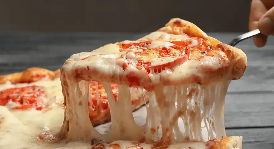 Rozciągający się, ciągnący ser na kawałku pizzy z pomidorami. Idealny przykład, jaki ser do pizzy wybrać, by uzyskać taki efekt.