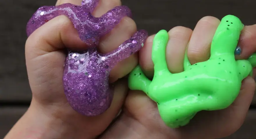 Hände formen lila Glitzer-Slime und grünen Schleim. So macht man Slime: Spaß für Kinder!