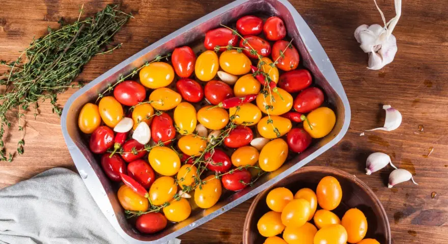 Pomodorini al forno rossi e gialli, aglio e peperoncino in una teglia, pronti per essere cotti.