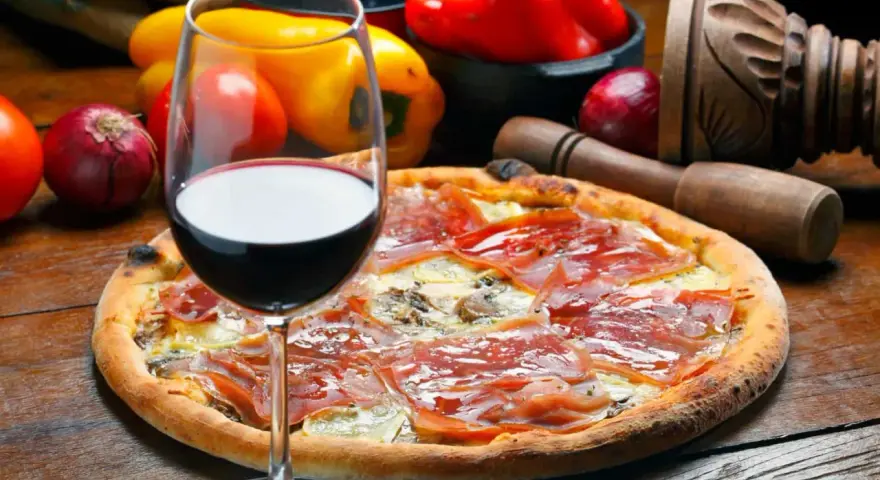 Idealne wino do pizzy, z kieliszkiem czerwonego wina i składnikami na pizze w tle.
