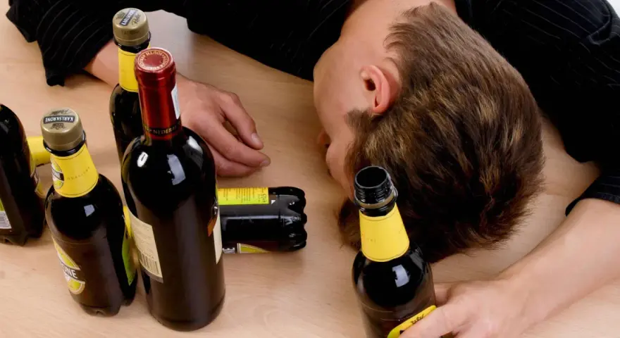 Ein Mann liegt bewusstlos auf einem Tisch, umgeben von leeren Flaschen. Der Gedanke, dass **Whisky gesund** sein könnte, ist hier wohl fehl am Platz.