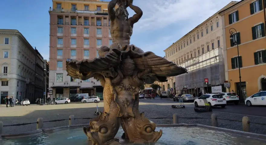 Fontana del Tritone in Piazza Barberini, Roma, con edifici storici e traffico sulla via dei Cappuccini.