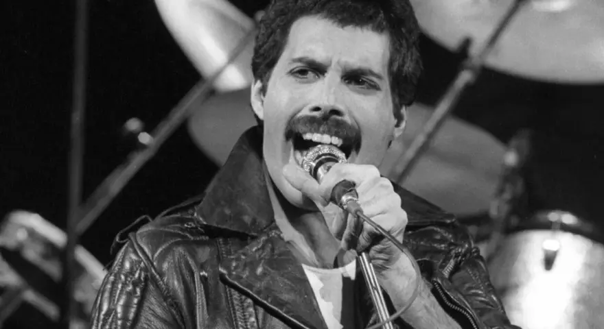 Freddie Mercury przed śmiercią, w skórzanej kurtce, śpiewa do mikrofonu. W tle widać perkusję.
