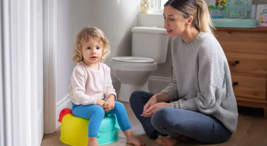 Mama uczy dziecko korzystać z nocnika. Mała dziewczynka siedzi na kolorowym nocniku, a mama siedzi obok, wspierając ją.