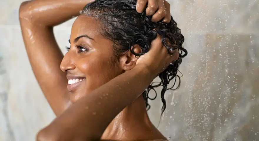 Frau wäscht sich unter der Dusche die Haare. Sie fragt sich, wie oft Haare waschen am besten ist.