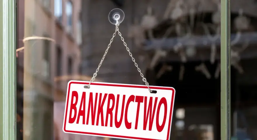 Tabliczka "BANKRUCTWO" wisząca na łańcuszku na szybie.