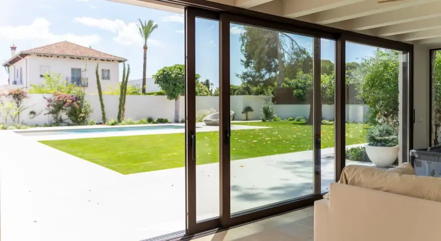 Amplias puertas correderas de cristal conectan el interior con un jardín con piscina, permitiendo una ventilación natural y la entrada de luz.