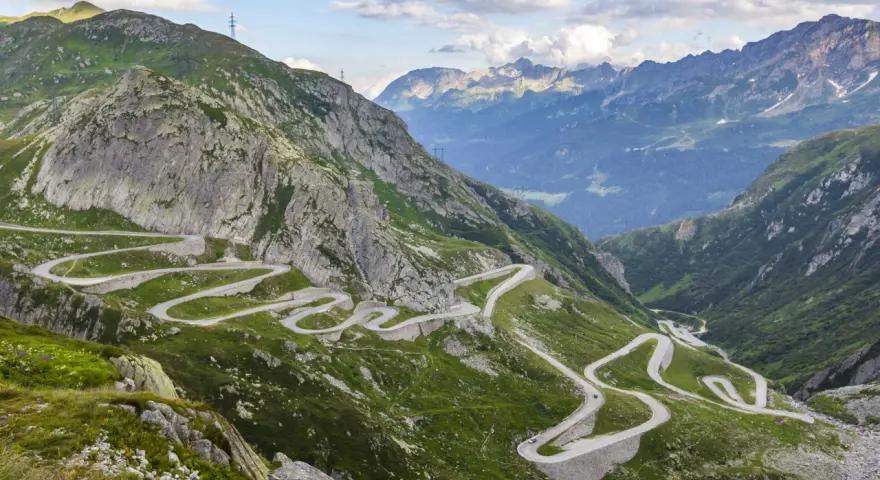 Strada tortuosa che sale sul passo Austria, circondata da montagne verdi e rocce imponenti.