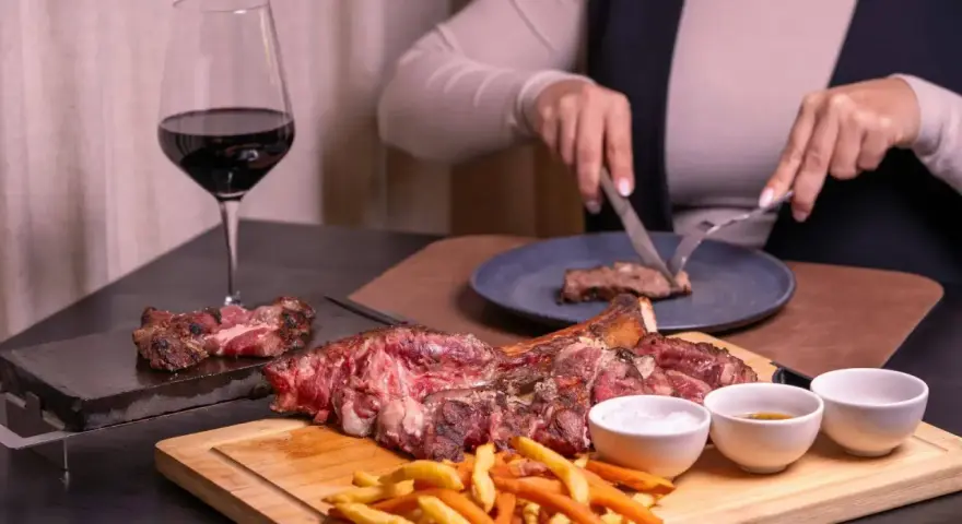 Idealne **jakie wino do wieprzowiny**? Czerwone wino i soczysta wieprzowina na desce, z frytkami i sosami.