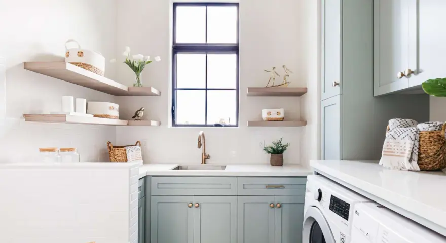 Stylish laundry room with mint cabinets, floating shelves, and a sink. This organized space shows how to organize laundry room with baskets and jars.