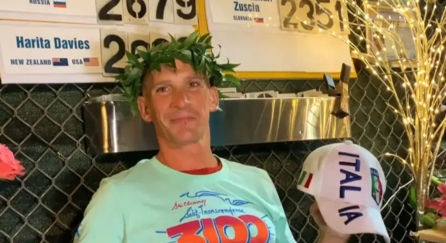 Vincitore con corona d'alloro, indossa una maglietta con scritto "3100" e un cappellino "ITALIA". Potrebbe essere un traguardo della ultramaratona più lunga del mondo.
