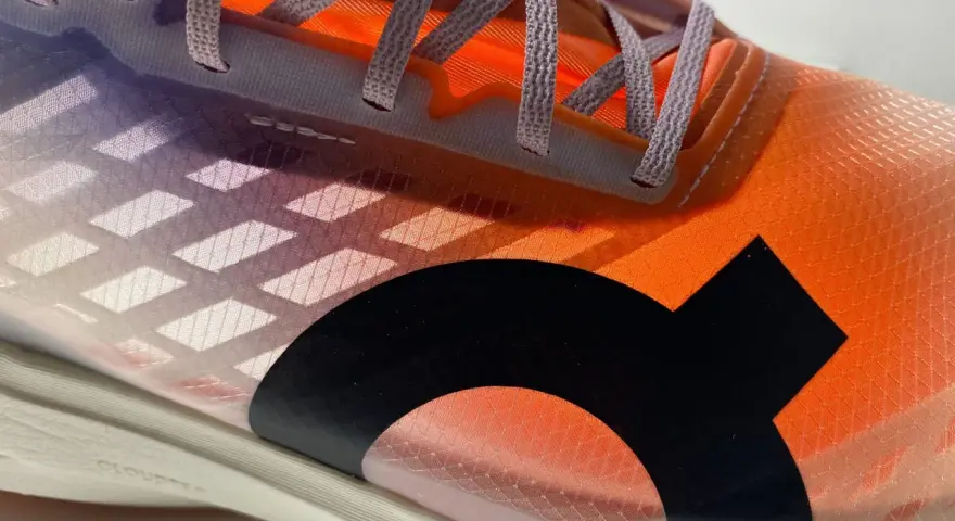 La tomaia di una scarpa da corsa arancione e viola con lacci grigi e un logo nero.