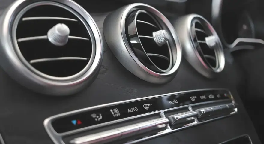 Trzy okrągłe nawiewy wentylacji w samochodzie, z pokrętłami do regulacji. Poniżej panel sterowania klimatyzacją, z przyciskami AUTO i MAX. Czekam na bardzo gorące powietrze z nawiewu.
