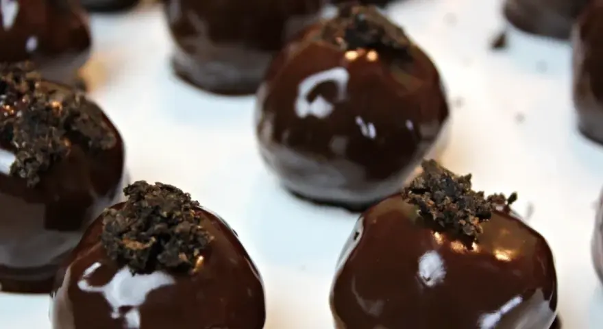 Deliziosi tartufini al cocco ricoperti di cioccolato fondente lucido, guarniti con briciole croccanti.
