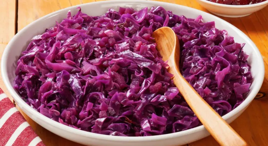 Col lombarda cocinada en un cuenco blanco con una cuchara de madera.