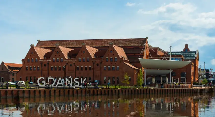 Gdańsk zwiedzanie: ceglane kamieniczki nad Motławą, wielki napis "GDAŃSK" i odbicie w wodzie.