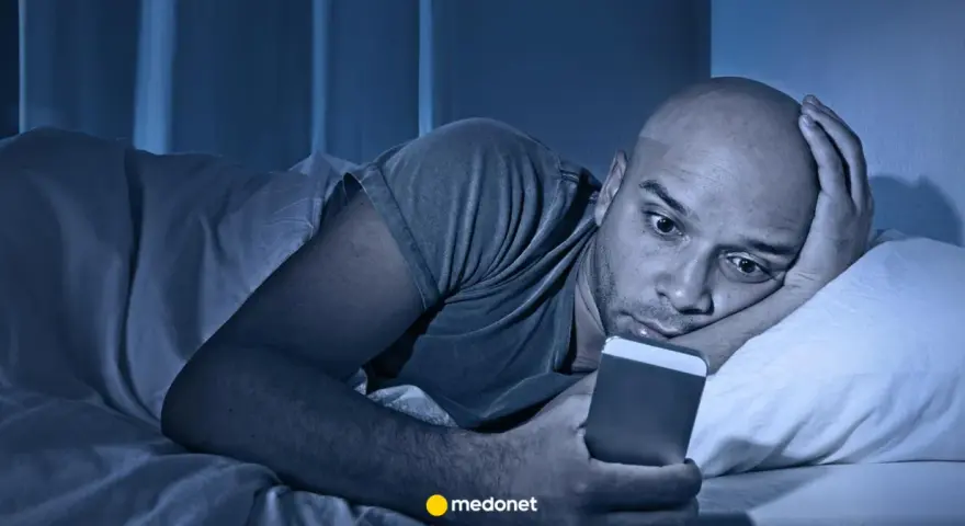 Mężczyzna leży w łóżku, wpatrując się w telefon. Czy to już obsesja?