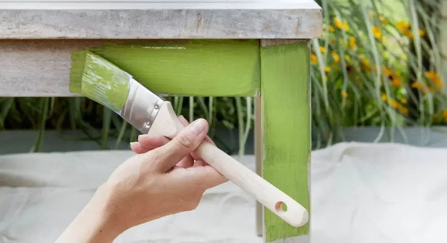 Mano pintando una mesa de madera con pintura verde brillante. El proceso de pintar con tizas da un acabado rústico y encantador.