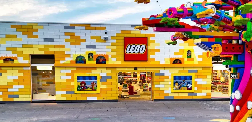 Bunte Lego-Steine schmücken das Gebäude und einen Baum. Ein lebendiger Lego-Freizeitpark lädt zum Spielen ein.