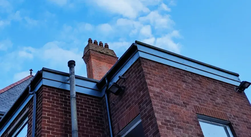 Vue d'une maison en briques rouges avec une cheminée traditionnelle et un conduit de poêle à bois sortie ventouse en façade. Ciel bleu avec quelques nuages.