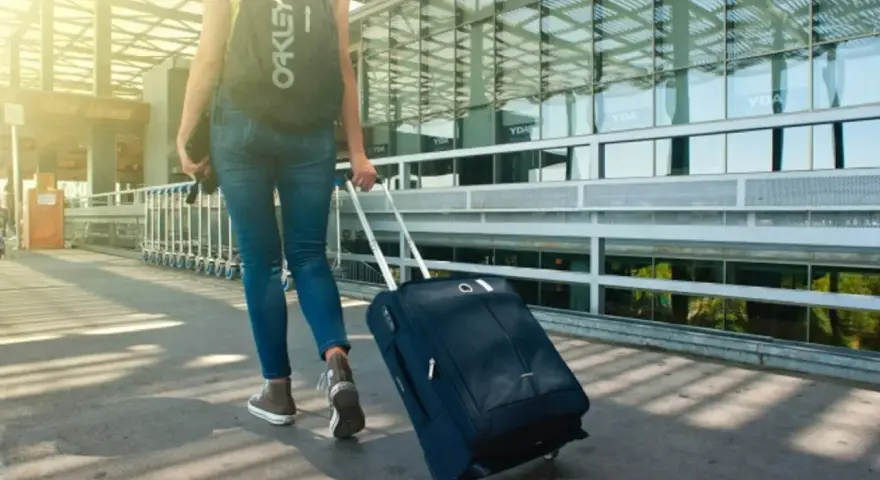 Kobieta z plecakiem Oakley ciągnie walizkę, zastanawiając się, ile może ważyć bagaż podręczny.
