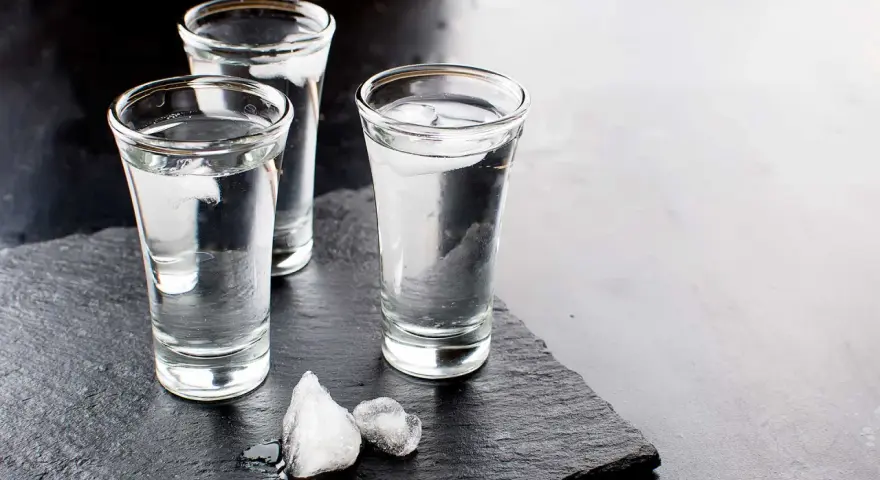 Drei Gläser Wodka mit Eiswürfeln auf dunklem Stein. Wodka wird aus Getreide oder Kartoffeln hergestellt.