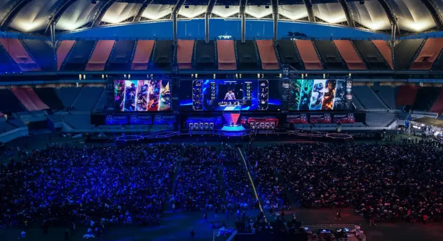 Wielki stadion wypełniony fanami oglądającymi transmisję z gry League of Legends. Na ekranach widać postacie i graczy, a tłum reaguje na emocjonujące rangi w lolu.