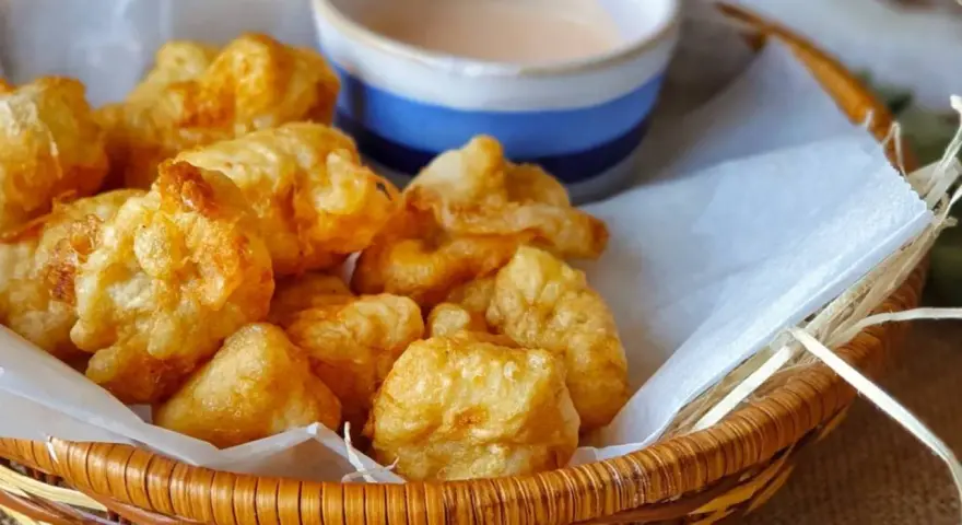 Cesta de mimbre con crujientes fritos de pixin, acompañados de una cremosa salsa rosa. ¡Un bocado delicioso!
