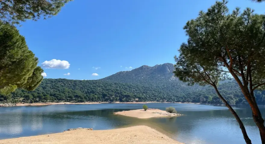 Piękna, piaszczysta plaża nad jeziorem w pobliżu Madrytu, otoczona sosnowym lasem i górami.