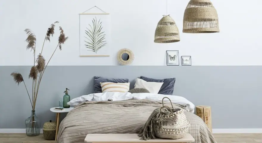 Sypialnia z łóżkiem i dwukolorową ścianą, pokazującą, jak połączyć dwa kolory na jednej ścianie. Wnętrze w stylu boho.