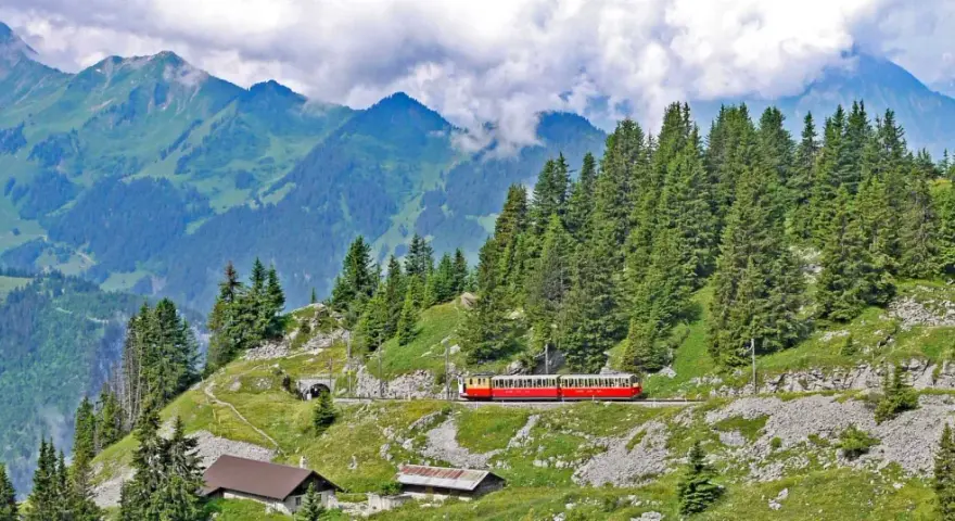 A red and yellow cogwheel train winds through the Swiss Alps, a scenic way to get around Interlaken.