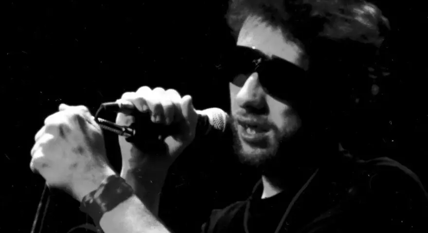 Chanteur d'un groupe irlandais punk, lunettes de soleil, micro en main, sur scène.