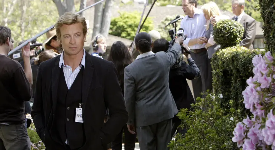 Simon Baker, con la sua nuova fidanzata, è circondato da telecamere e microfoni durante un evento all'aperto.