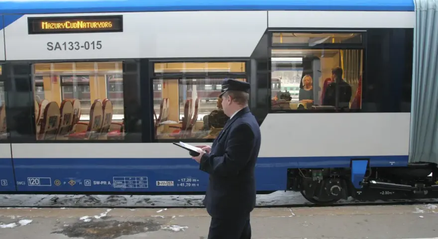 Konduktor sprawdza dane na tablecie. Zastanawiasz się, ile kosztuje bilet u konduktora? Wnętrze pociągu z siedzeniami.