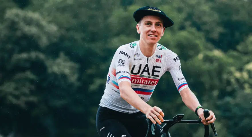 Tadej Pogačar, known for his incredible VO2 max, smiles while riding his bike in a UAE Emirates jersey and a Basque beret.