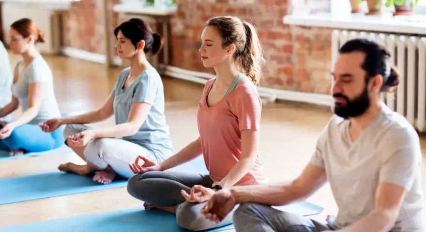 Menschen in einem Yogastudio praktizieren Stress-Meditation, sitzen im Lotussitz auf Matten und schließen die Augen.
