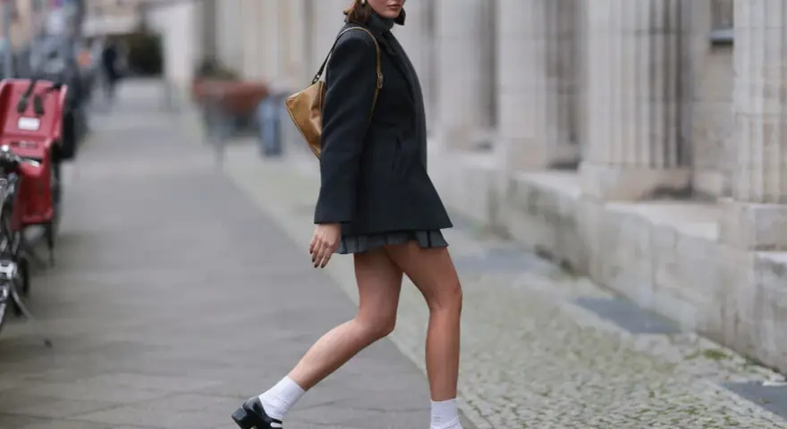 Dziewczyna w stylu Marry Jane, w szarej beretce i krótkiej spódniczce, idzie ulicą.