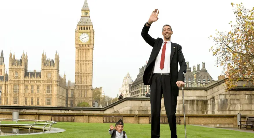 Der größte Mensch der Welt winkt vor dem Big Ben in London. Neben ihm steht ein Mann von sehr kleinem Wuchs.