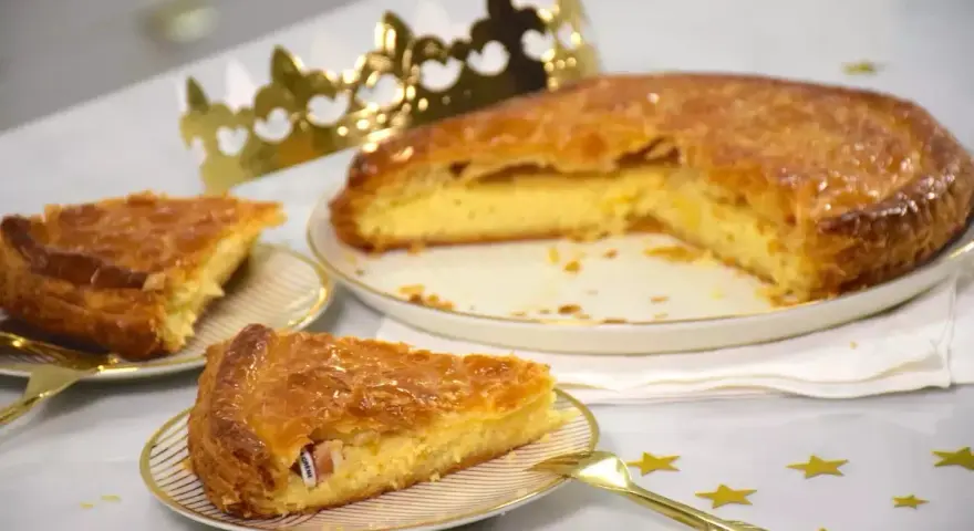 Une galette de farine dorée, prête à être dégustée, avec une fève cachée dans une part. Une couronne dorée trône à côté, promesse de fête.