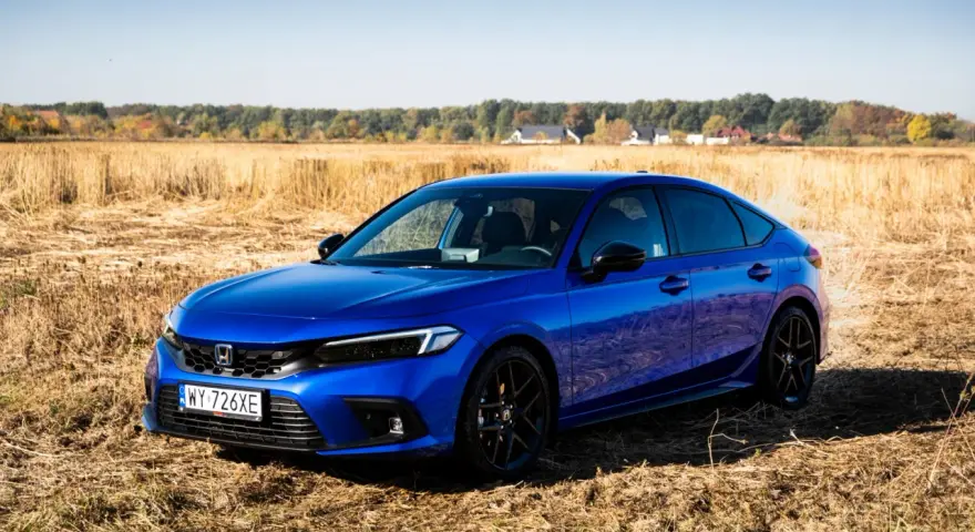 Błękitny Honda Civic 11. generacji na tle jesiennego pola.