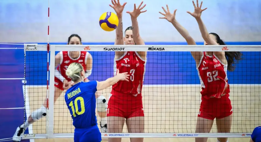 Piłka leci nad siatką podczas meczu liga światowa w piłce siatkowej. Zawodniczki w czerwonych strojach próbują ją zablokować.
