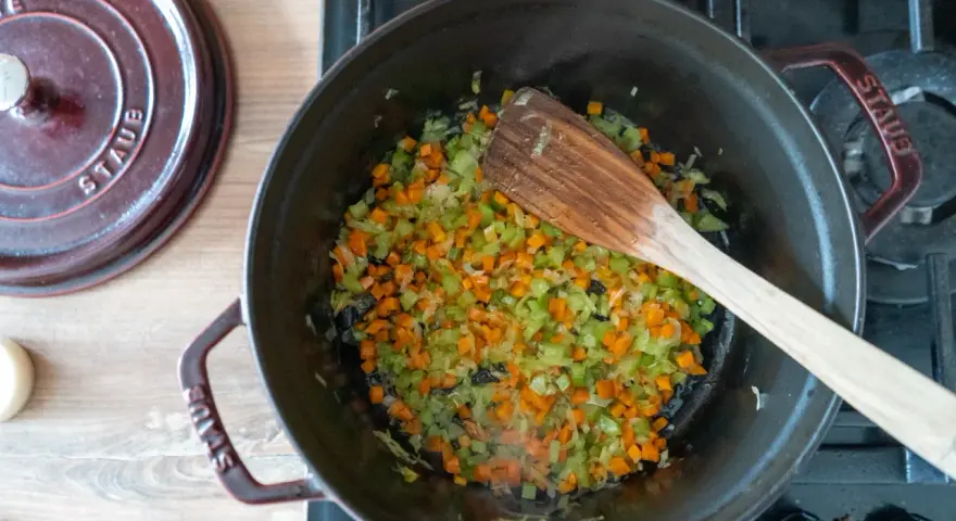 Würfel aus Karotten, Sellerie und Zwiebeln werden in einem Topf für ein soffritto rezept angedünstet.