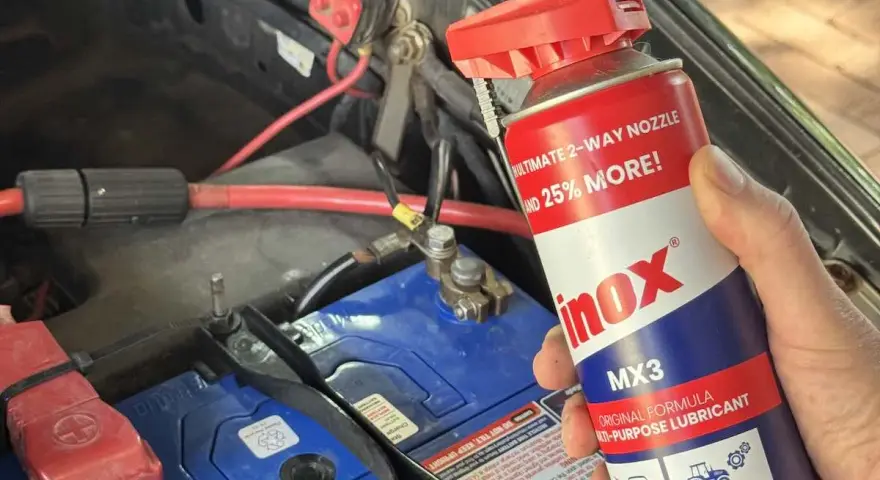 A hand holds a can of INOX MX3 lubricant near a car battery. Does cleaning battery terminals help? This spray might be the answer.