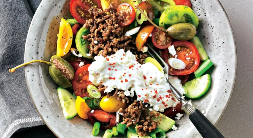 Bunter Tomatensalat mit Feta, Hackfleisch und Kapern. Frische Tomaten, Gurken und Frühlingszwiebeln bilden die Basis für diesen herzhaften Salat.