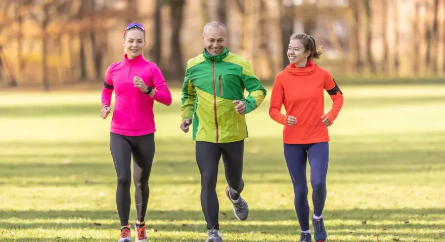 Un gruppo di amici sorridenti segue un programma allenamento corsa e camminata in un parco autunnale.