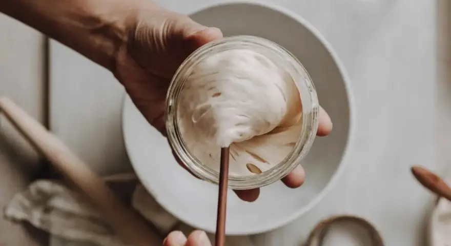Eine Hand hält ein Glas mit lebendigem Sauerteig, bereit zum Auffrischen. Blasen und Luftlöcher zeigen seine Aktivität.