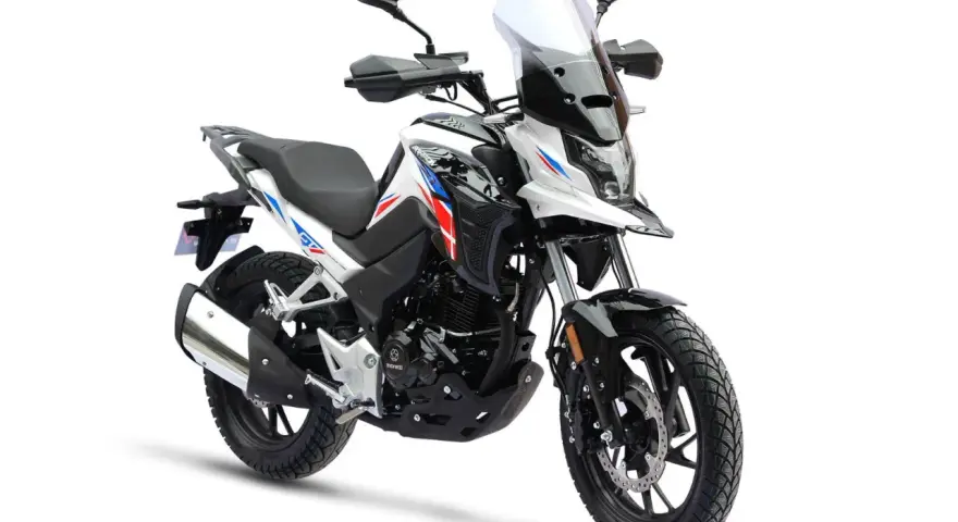 Nowy motocykl gotowy do docierania. Biało-czarny z czerwono-niebieskimi akcentami, z wysoką szybą i terenowymi oponami.