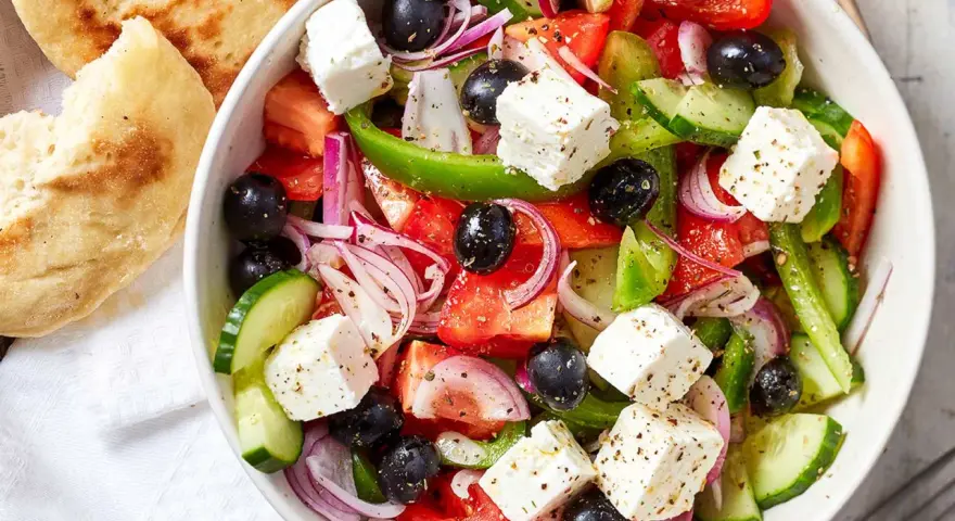 Frischer griechischer Salat mit Tomaten, Gurken, roten Zwiebeln, Oliven und Feta-Käse, serviert mit Fladenbrot.