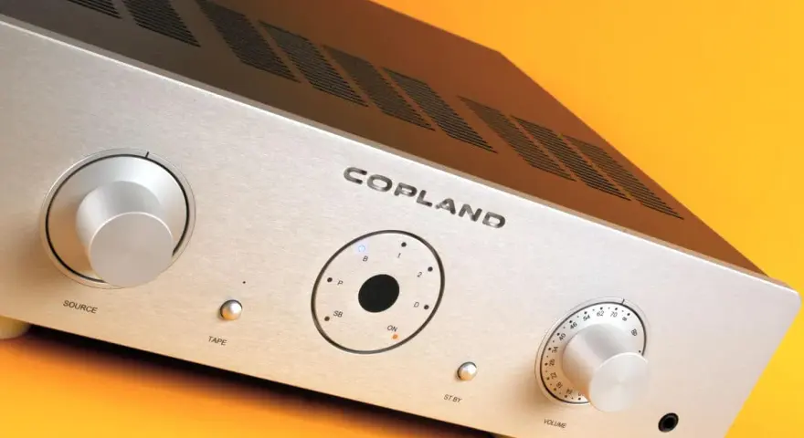 Srebrny wzmacniacz Copland CSA 100 z pokrętłami Source i Volume, przyciskiem Tape oraz wskaźnikami.